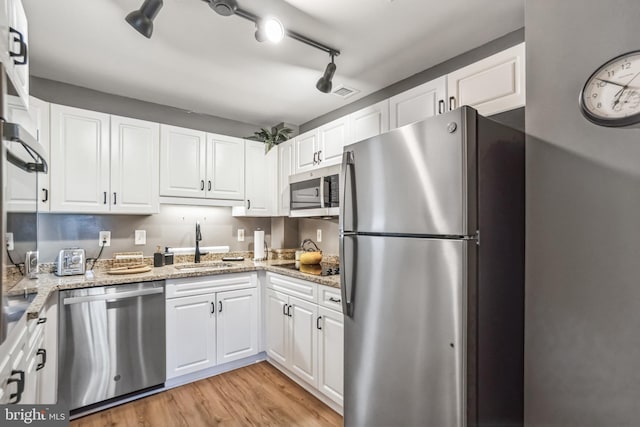 kitchen with stainless steel appliances, white cabinetry, light stone countertops, and light wood-type flooring