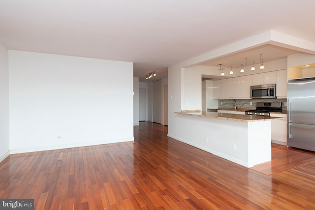 kitchen featuring hardwood / wood-style floors, white cabinets, backsplash, kitchen peninsula, and stainless steel appliances