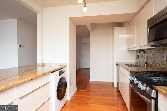 kitchen featuring washer / dryer, sink, white cabinetry, stainless steel appliances, and light stone countertops