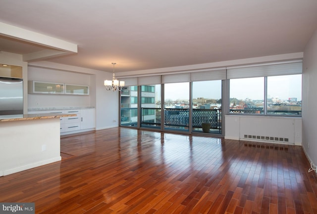 unfurnished living room with plenty of natural light, dark wood-type flooring, and an inviting chandelier