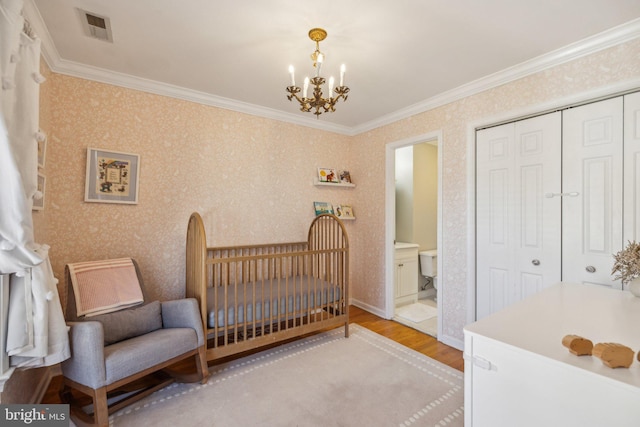 bedroom with an inviting chandelier, light hardwood / wood-style flooring, ornamental molding, a closet, and a crib