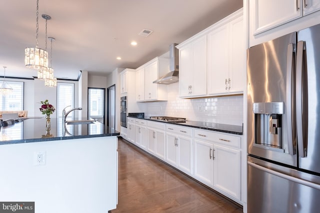 kitchen with a sink, visible vents, appliances with stainless steel finishes, wall chimney exhaust hood, and dark wood finished floors