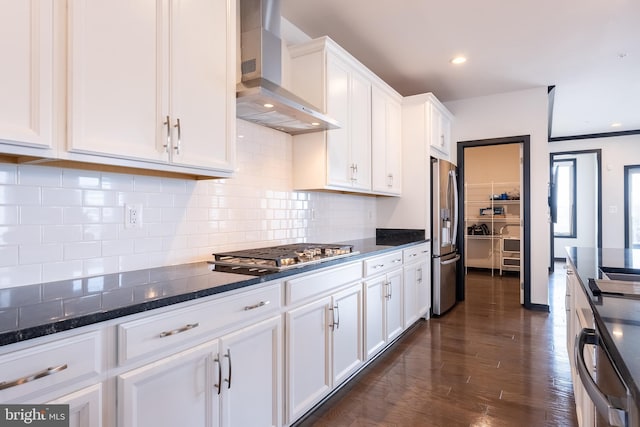 kitchen featuring stainless steel appliances, white cabinetry, wall chimney range hood, backsplash, and dark wood-style floors