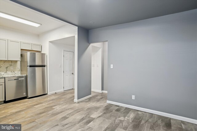 kitchen featuring backsplash, light stone counters, light hardwood / wood-style flooring, and appliances with stainless steel finishes