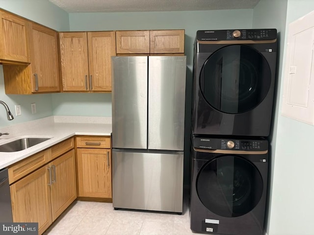 kitchen with sink, stainless steel fridge, stacked washer / dryer, a textured ceiling, and light tile patterned flooring