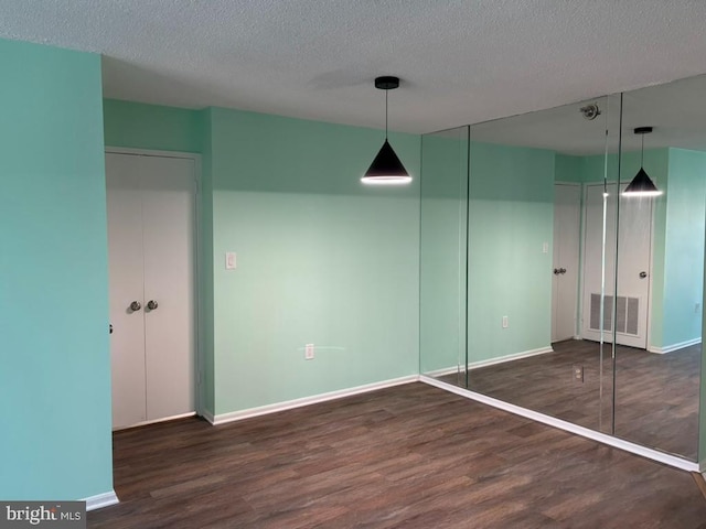 interior space featuring hanging light fixtures, dark wood-type flooring, and a textured ceiling