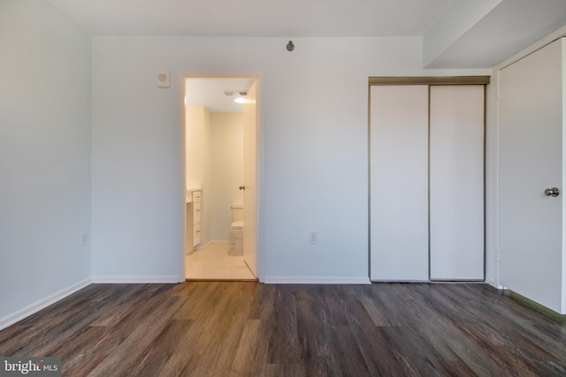 unfurnished bedroom featuring connected bathroom, dark wood-type flooring, and a closet