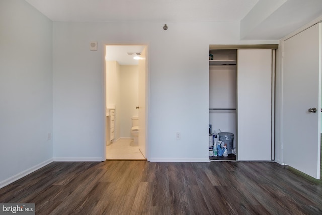 unfurnished bedroom with connected bathroom, dark hardwood / wood-style flooring, and a closet