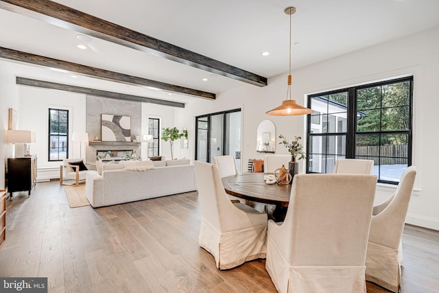 dining room featuring beam ceiling, a premium fireplace, and light wood-type flooring