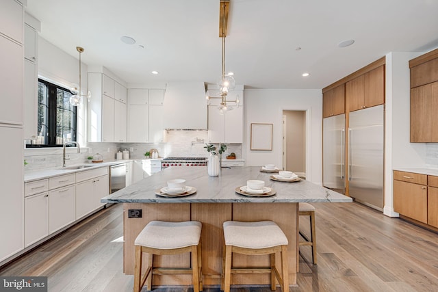 kitchen with pendant lighting, sink, white cabinets, built in refrigerator, and a center island