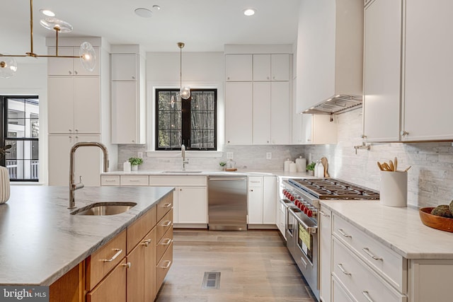 kitchen featuring white cabinetry, sink, stainless steel appliances, light stone countertops, and wall chimney range hood