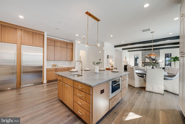 kitchen with appliances with stainless steel finishes, decorative light fixtures, sink, light hardwood / wood-style floors, and a center island with sink