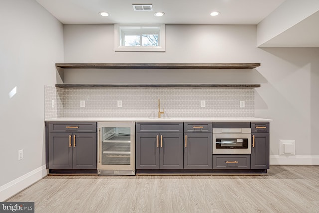 bar featuring gray cabinets, sink, oven, wine cooler, and light wood-type flooring