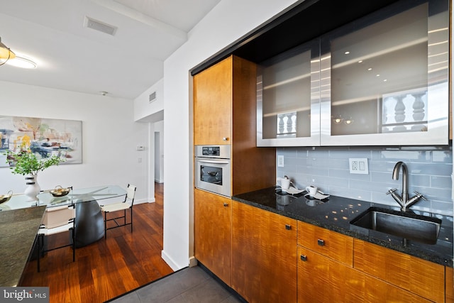 kitchen with dark stone countertops, sink, tasteful backsplash, and stainless steel oven