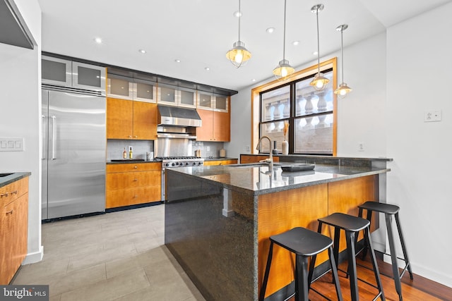 kitchen with sink, a kitchen breakfast bar, high quality appliances, decorative light fixtures, and dark stone counters