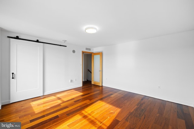 unfurnished bedroom with wood-type flooring, a barn door, and a closet