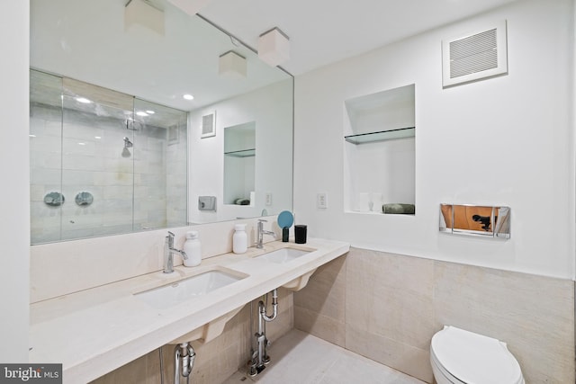 bathroom with tile walls, double sink, toilet, and walk in shower