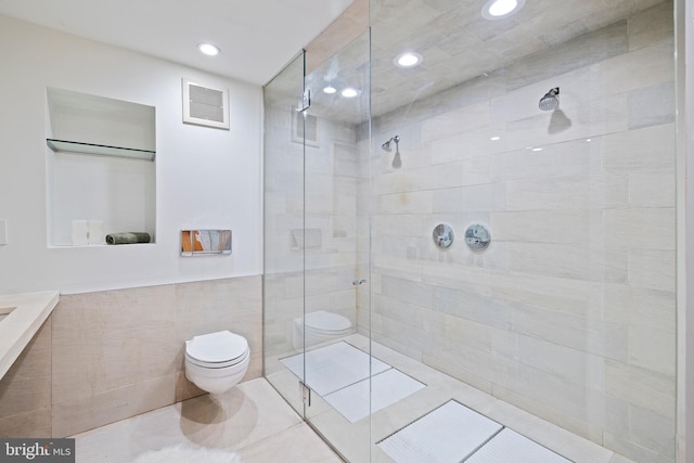 bathroom featuring a tile shower, tile patterned floors, tile walls, and toilet