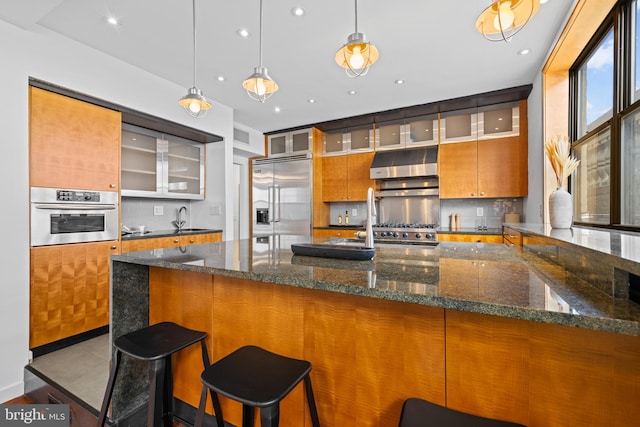 kitchen featuring pendant lighting, appliances with stainless steel finishes, range hood, and dark stone counters