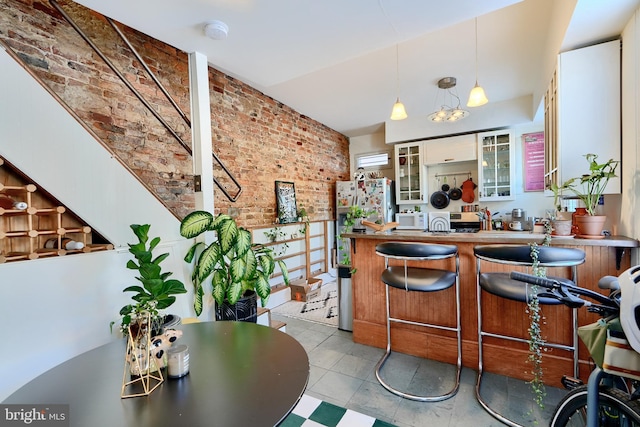 bar featuring decorative light fixtures, brick wall, stainless steel fridge, and white cabinetry