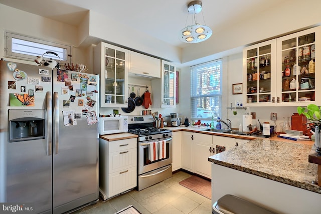 kitchen with light stone countertops, appliances with stainless steel finishes, white cabinetry, sink, and pendant lighting