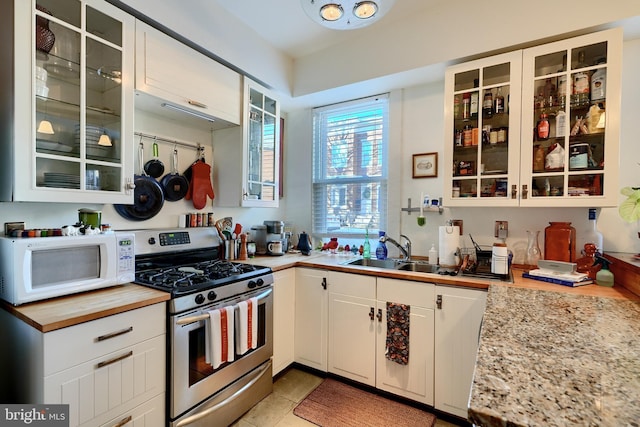 kitchen featuring gas range, sink, white cabinets, light stone counters, and light tile patterned flooring