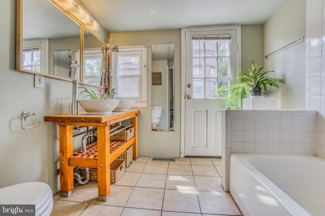 bathroom featuring a wealth of natural light, toilet, a bathing tub, and tile patterned flooring