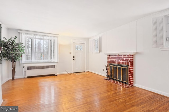 unfurnished living room featuring crown molding, a brick fireplace, radiator, and light hardwood / wood-style flooring