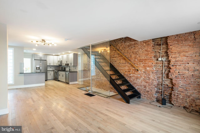 unfurnished living room with sink, light wood-type flooring, and brick wall