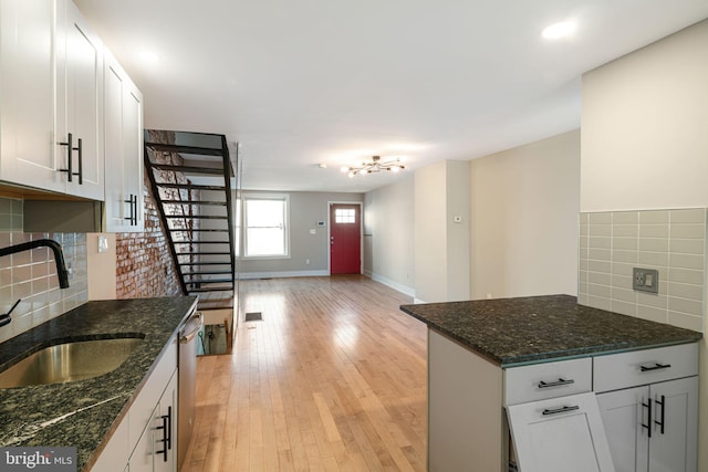 kitchen with sink, backsplash, white cabinets, light wood-type flooring, and dark stone counters