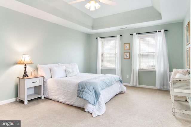 bedroom with a raised ceiling, light colored carpet, ceiling fan, and multiple windows