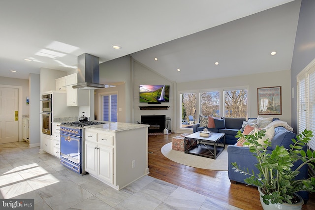 kitchen with vaulted ceiling, white cabinetry, island exhaust hood, light stone counters, and stainless steel appliances