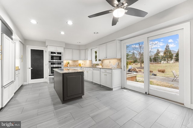 kitchen with white cabinetry, light stone counters, a kitchen island, stainless steel double oven, and decorative backsplash