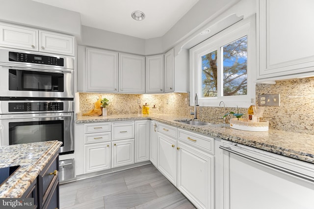 kitchen featuring tasteful backsplash, white cabinets, light stone countertops, and stainless steel double oven