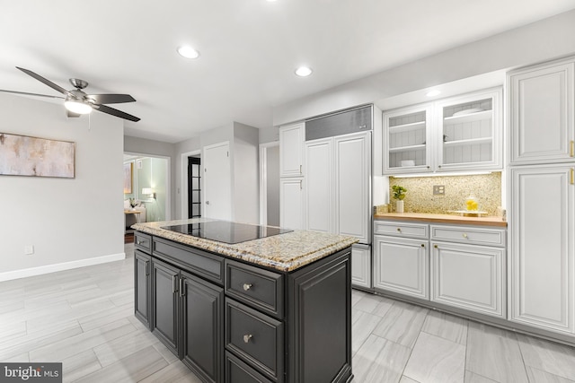 kitchen with white cabinetry, black electric cooktop, a kitchen island, ceiling fan, and backsplash