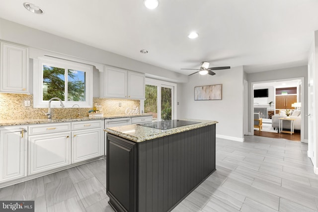 kitchen featuring light stone counters, a center island, white cabinets, black electric stovetop, and backsplash