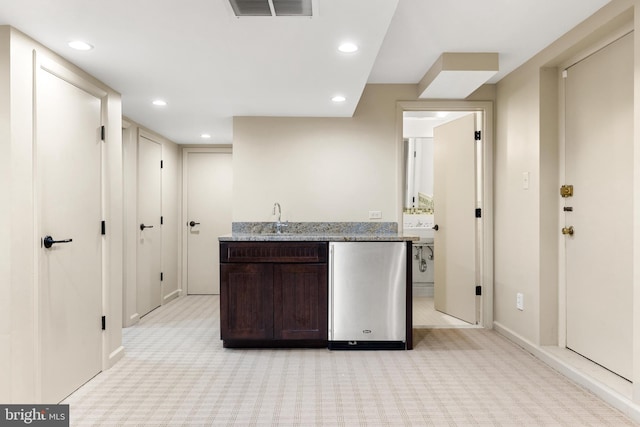 kitchen featuring sink, light colored carpet, light stone counters, and dark brown cabinetry