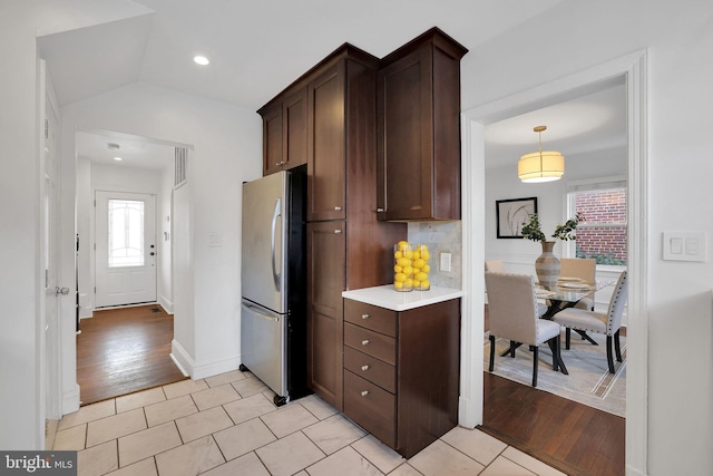 kitchen with dark brown cabinets, a healthy amount of sunlight, stainless steel refrigerator, and decorative backsplash