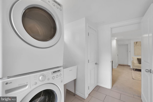 clothes washing area featuring light tile patterned floors and stacked washing maching and dryer