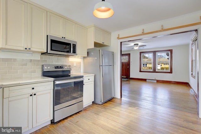 kitchen featuring baseboard heating, stainless steel appliances, tasteful backsplash, cream cabinets, and light wood-type flooring