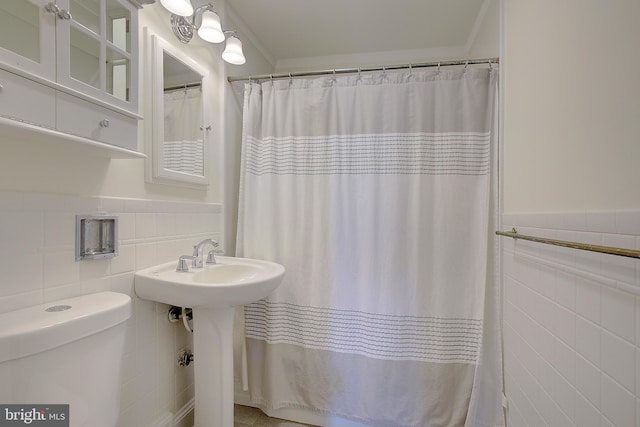 bathroom featuring ornamental molding, toilet, sink, and tile walls