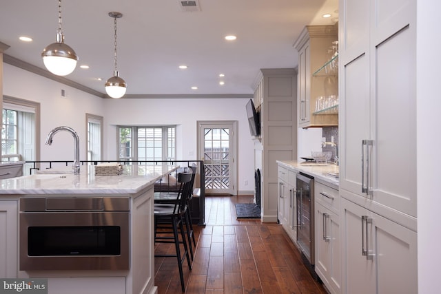 kitchen with a center island with sink, white cabinets, light stone countertops, and dark hardwood / wood-style flooring