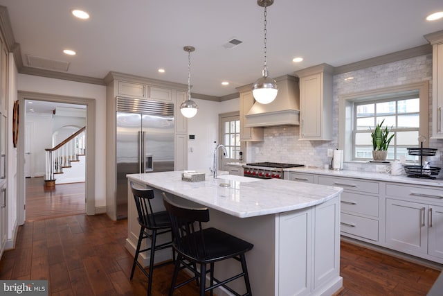 kitchen featuring light stone countertops, stainless steel appliances, hanging light fixtures, dark hardwood / wood-style floors, and a kitchen island with sink