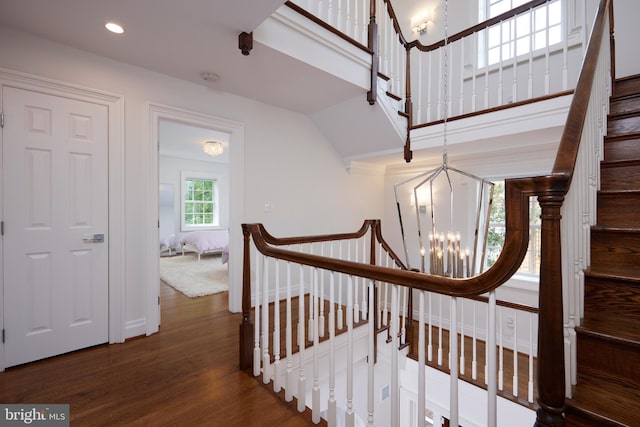 stairway with a notable chandelier, lofted ceiling, and wood-type flooring