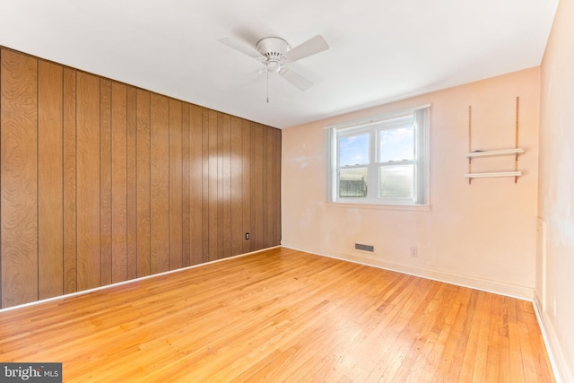 unfurnished room featuring ceiling fan, wooden walls, and light hardwood / wood-style floors