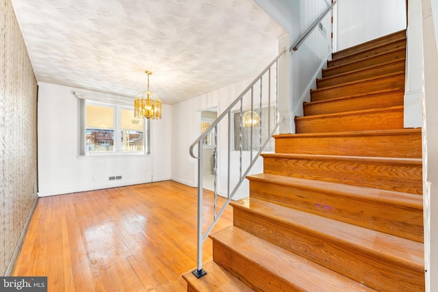 stairway with hardwood / wood-style floors and a notable chandelier