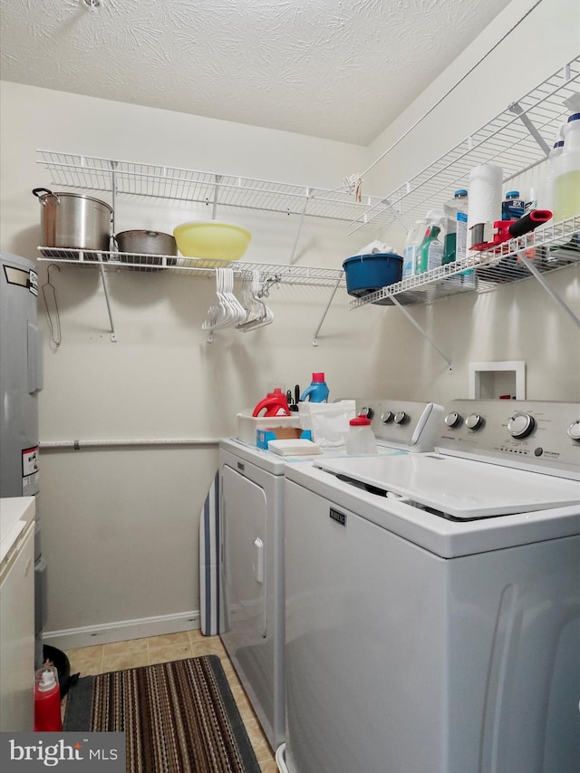 clothes washing area featuring light tile patterned floors, a textured ceiling, electric water heater, and washing machine and clothes dryer