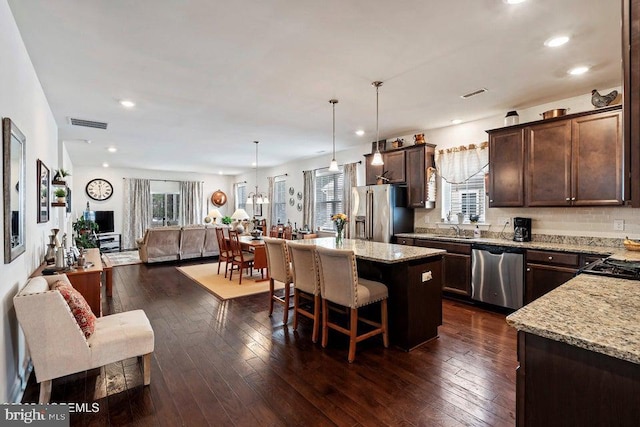 kitchen with light stone countertops, pendant lighting, appliances with stainless steel finishes, a center island, and dark hardwood / wood-style floors