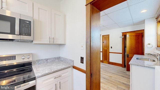 kitchen with sink, stainless steel appliances, light stone countertops, white cabinets, and a drop ceiling