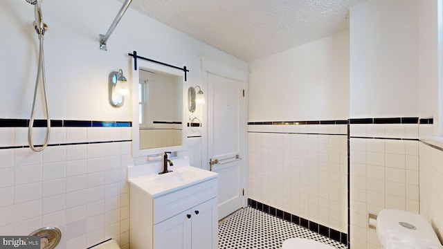 bathroom with tile walls, vanity, toilet, and a textured ceiling